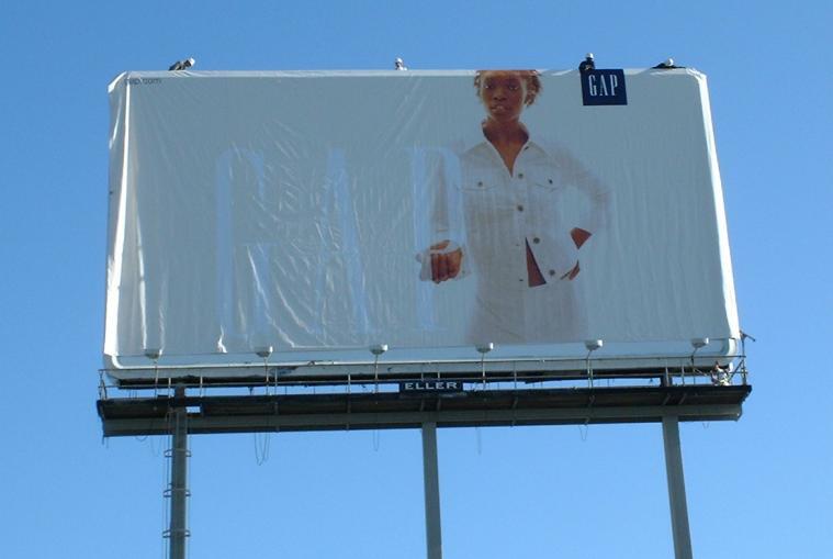 Ein riesiges (etwa 35 mal 15 Meter) Reklameschild am Rand der Autobahn. Vergrößert das Bild und ihr seht die vier behelmten Arbeiter ganz oben, wie sie das Material festzurren!